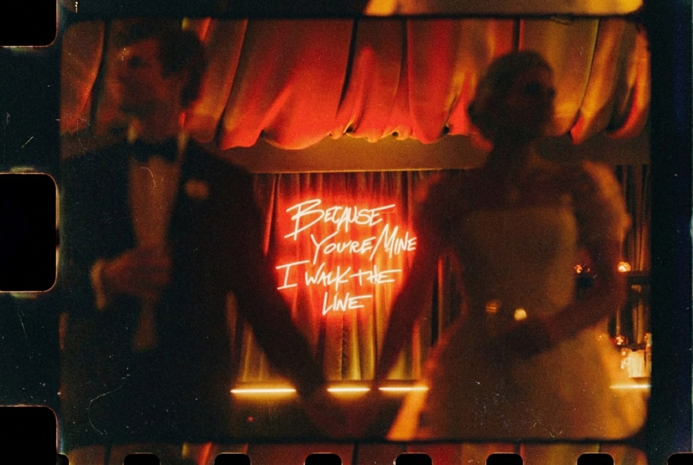 Neon noir on 35mm. The red light is allowed to blow, and the couple stays legible at the edges.
